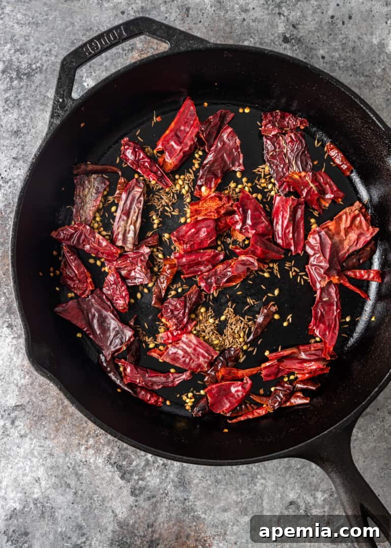 Dried chiles and spices being dry roasted in a skillet over medium heat, releasing their aromas.