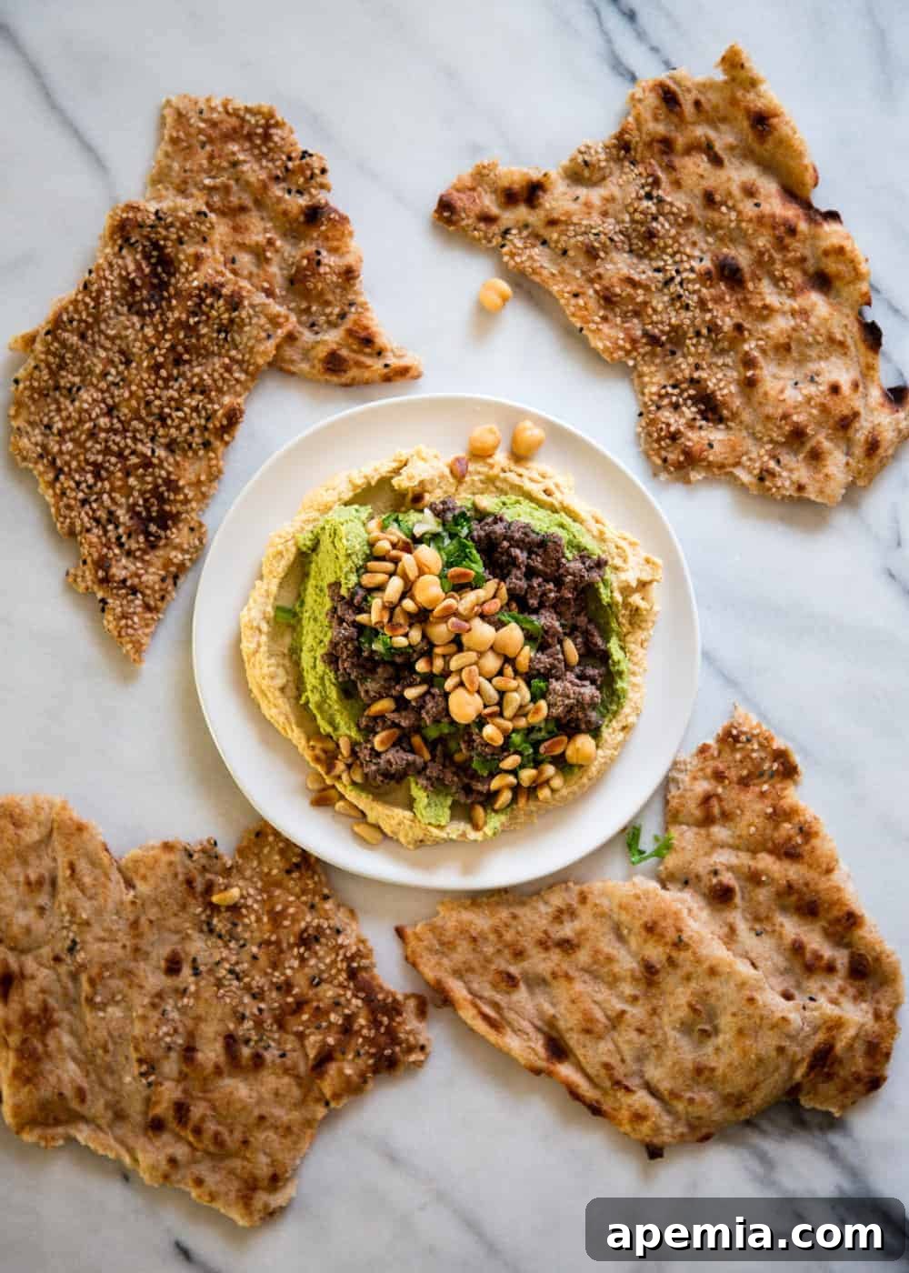 overhead image of hummus kawarma, surrounded by seeded flatbread crackers