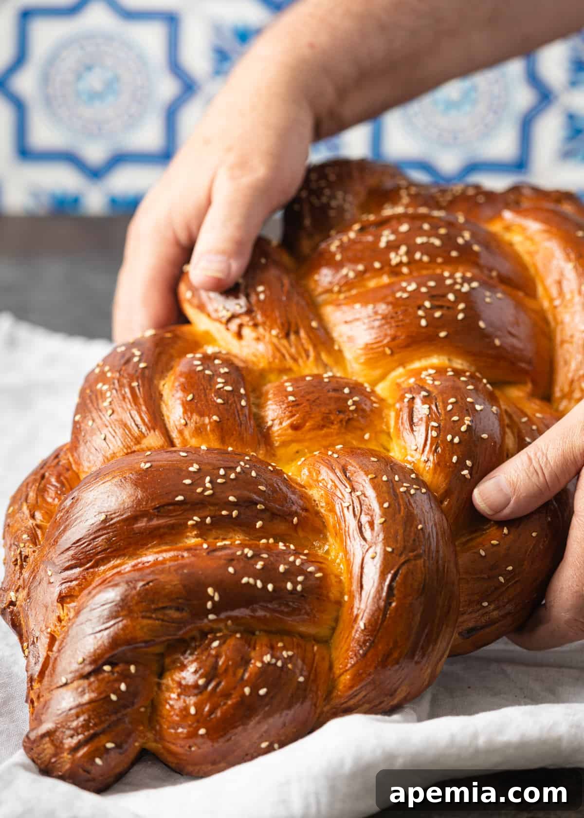 Close-up shot of hands gently lifting a freshly baked Challah loaf from a tea towel, highlighting its golden crust and soft texture.