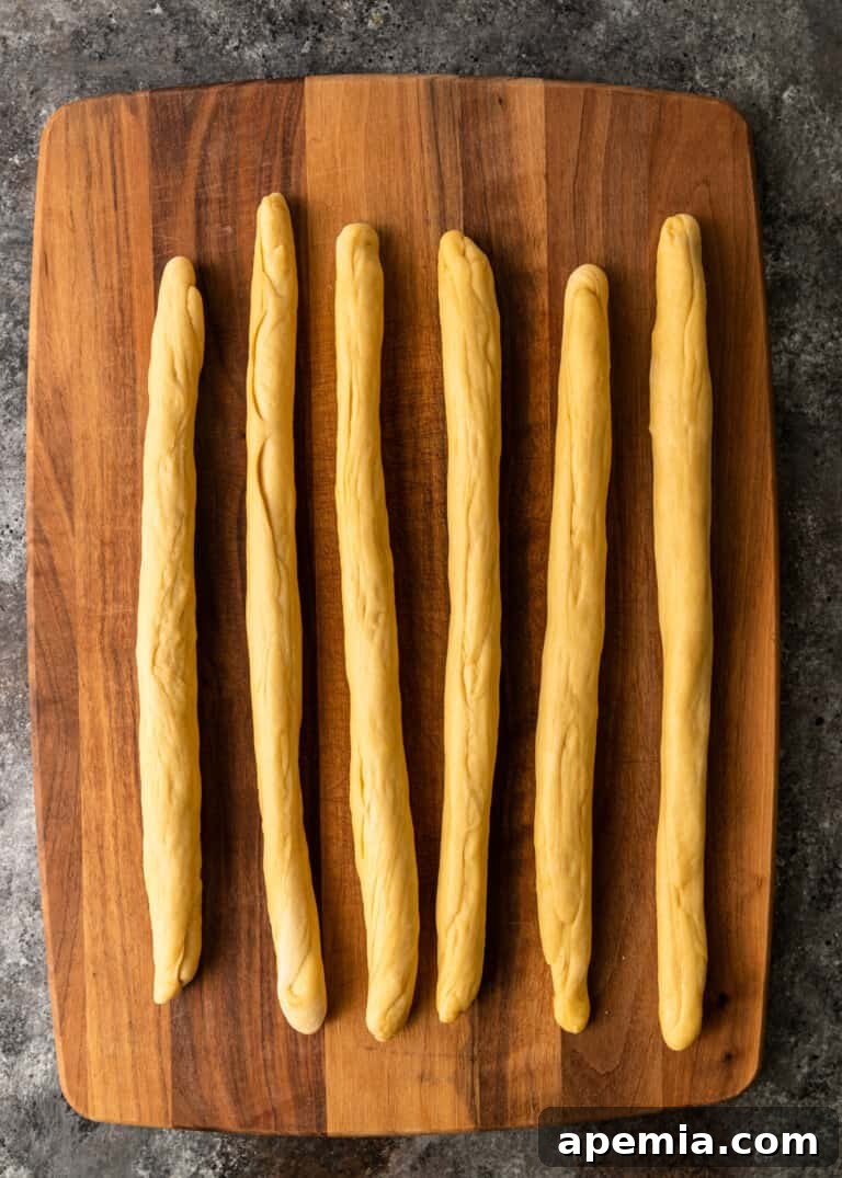 Process shot: Six pieces of Challah dough rolled out to 18-inch ropes on a cutting board, ready for braiding.