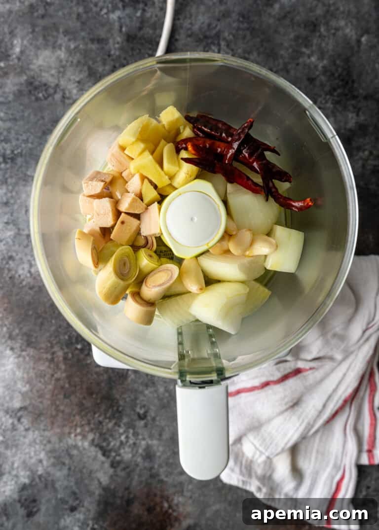 Overhead process shot demonstrating the blending of curry paste ingredients in a food processor, capturing the initial stage of preparation.