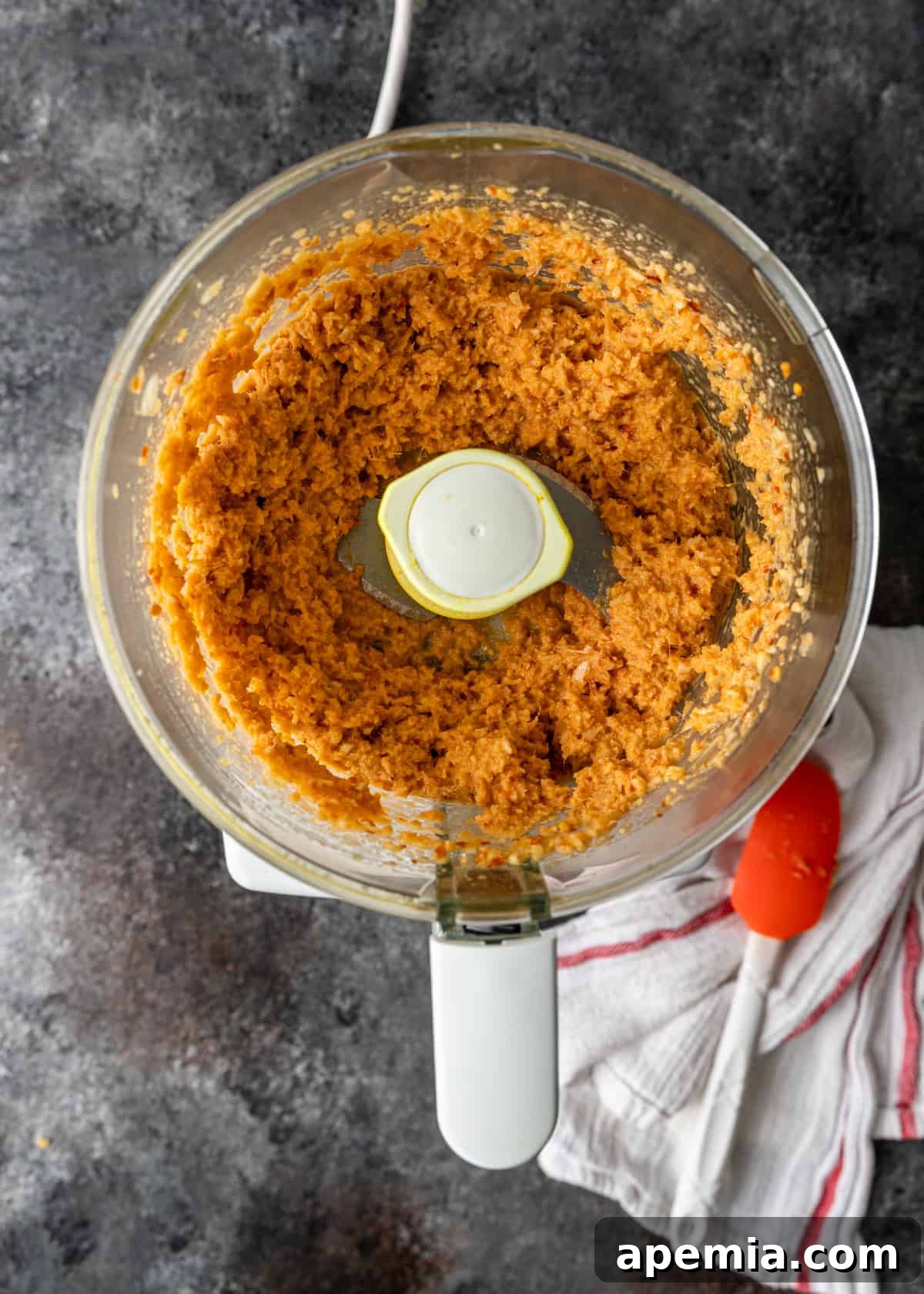 Overhead process shot showing the finely chopped and blended ingredients for the curry paste within a food processor bowl, highlighting its smooth texture.