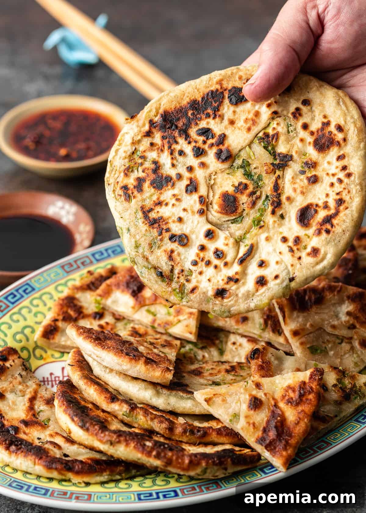 a hand holding a freshly cooked scallion pancake, showing its flaky layers