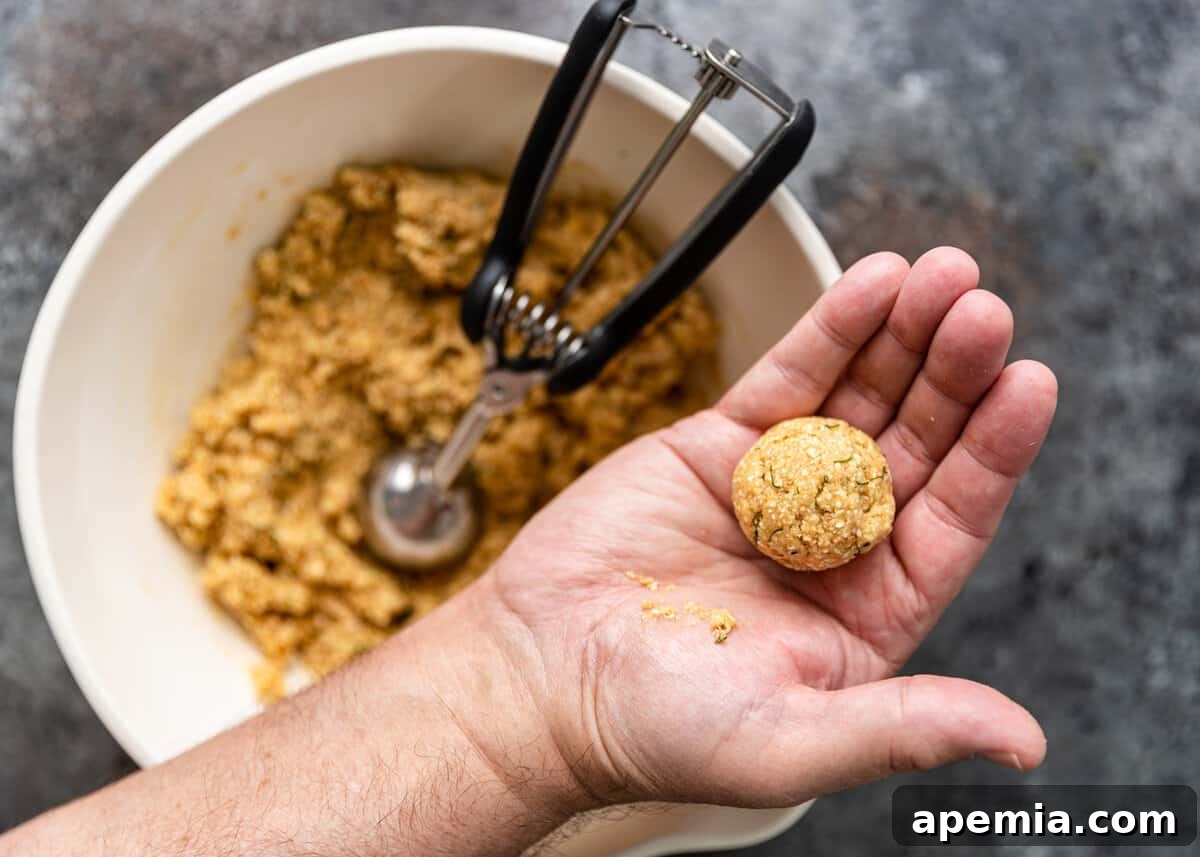 overhead closeup: hand holding formed matzo ball overtop of mixing bowl with remaining ingredients with scooper