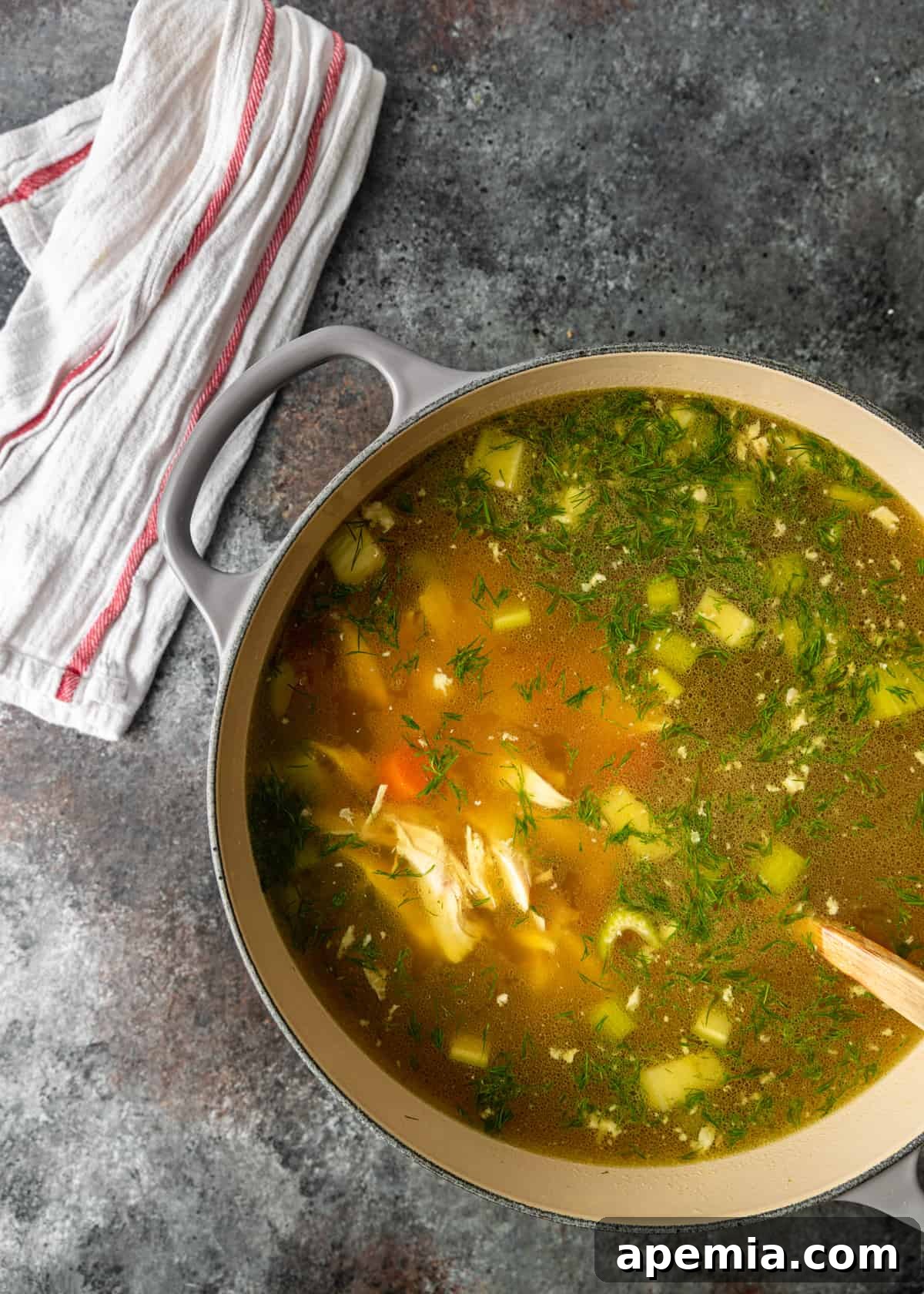 overhead: matzo ball soup in a pot on countertop with white linen off to side