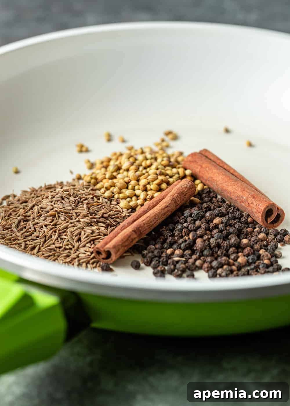 Close-up photo of whole cinnamon sticks, fennel seeds, black peppercorns, and sumac berries in a white bowl, showcasing Baharat's key ingredients.