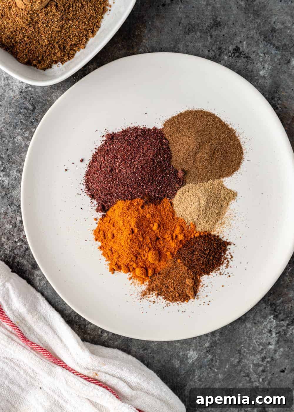 Six different Arabic ground spices arranged artfully on a white plate, ready to be blended into Baharat.