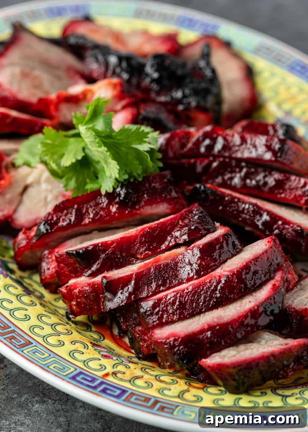Close-up of thin slices of ruby-red Char Siu barbecue pork arranged artfully on a platter, highlighting its beautiful texture and glaze.