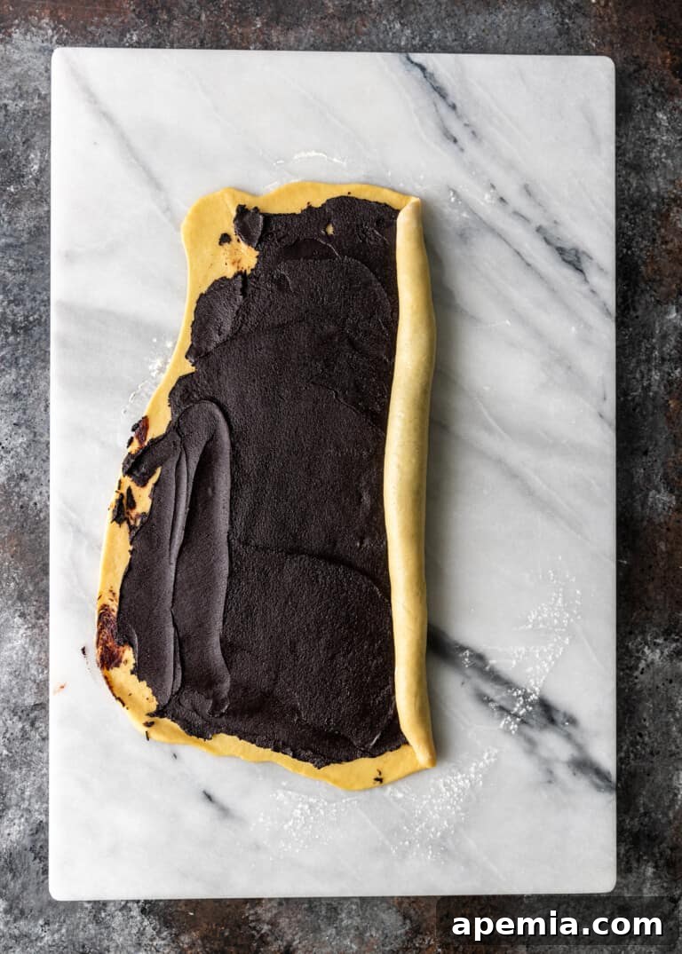 Overhead process shot: Babka dough with chocolate filling being carefully rolled into a tight log.