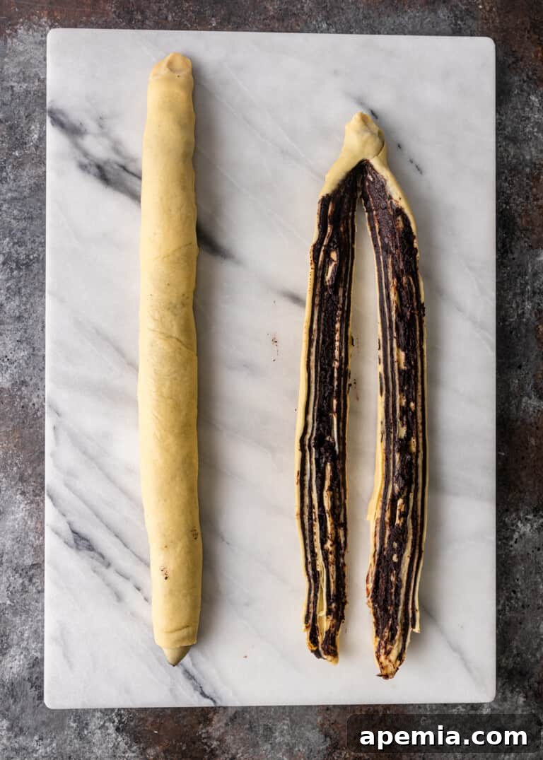 Overhead process shot: Two chocolate babka logs, one of which has been sliced lengthwise to reveal the chocolate layers.