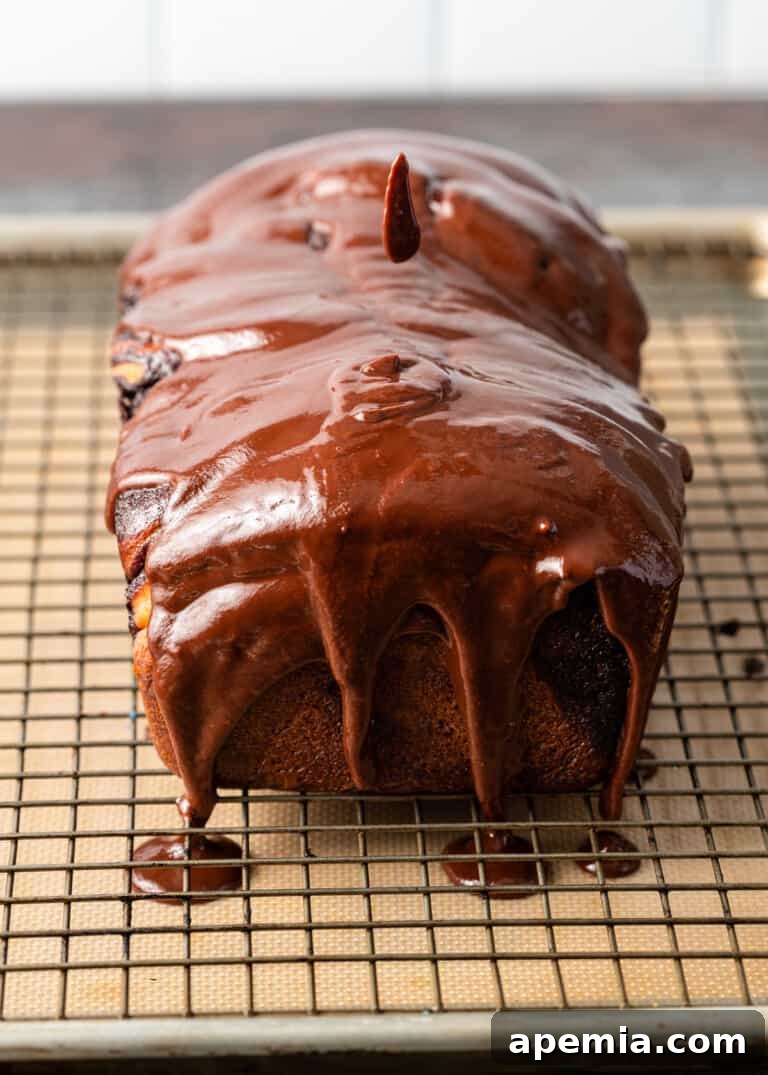 Overhead process shot: Baked babka with chocolate glaze fully applied, dripping slightly onto the baking sheet below.