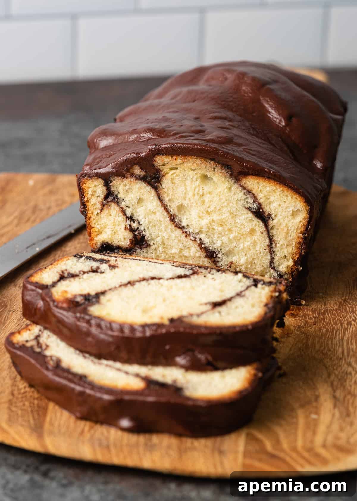 Close-up view of a whole chocolate babka with two slices cut and placed on the side, sitting on a wooden cutting board with a knife.