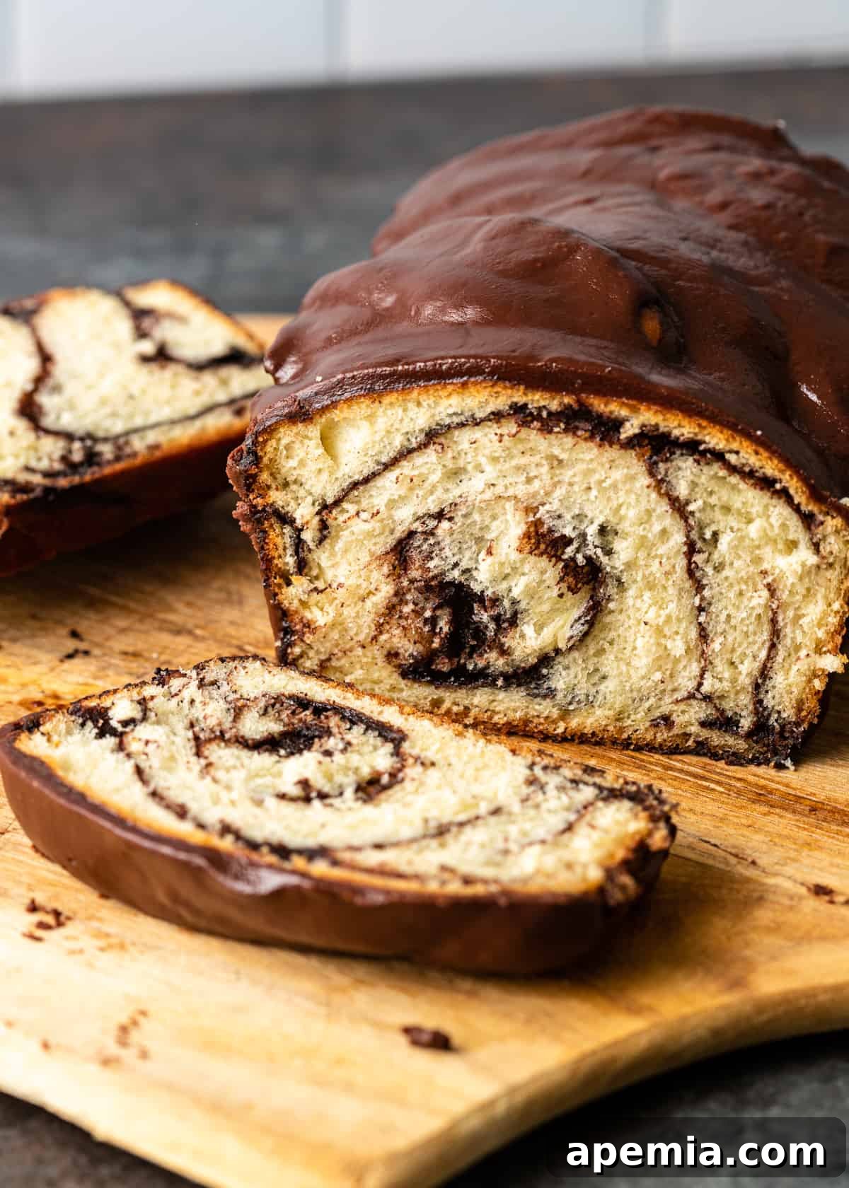 Close-up view of a baked chocolate babka, with several sliced pieces artfully arranged beside it on a wooden cutting board.