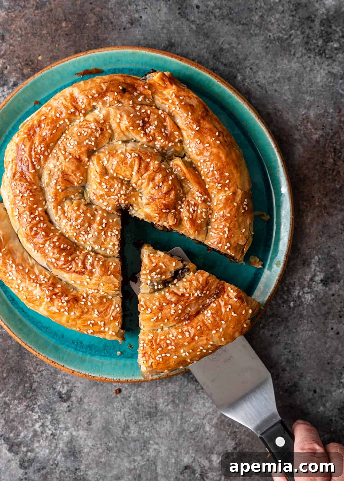 overhead: a spatula lifting a slice of bourekas from the full meat filled pastry