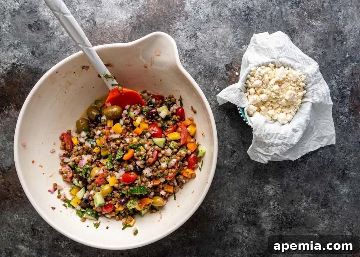 overhead: cheese in small bowl in paper towel off to the side of large pouring bowl of Greek lentil salad