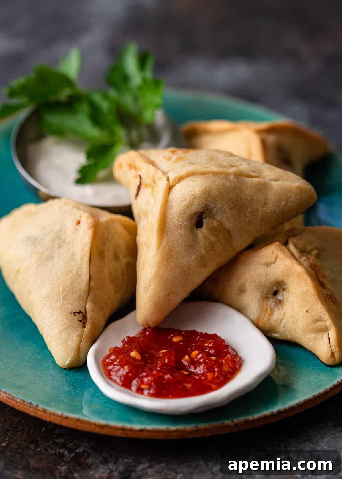 closeup: stack of hasweh hand pies on a blue plate with red shatta sauce