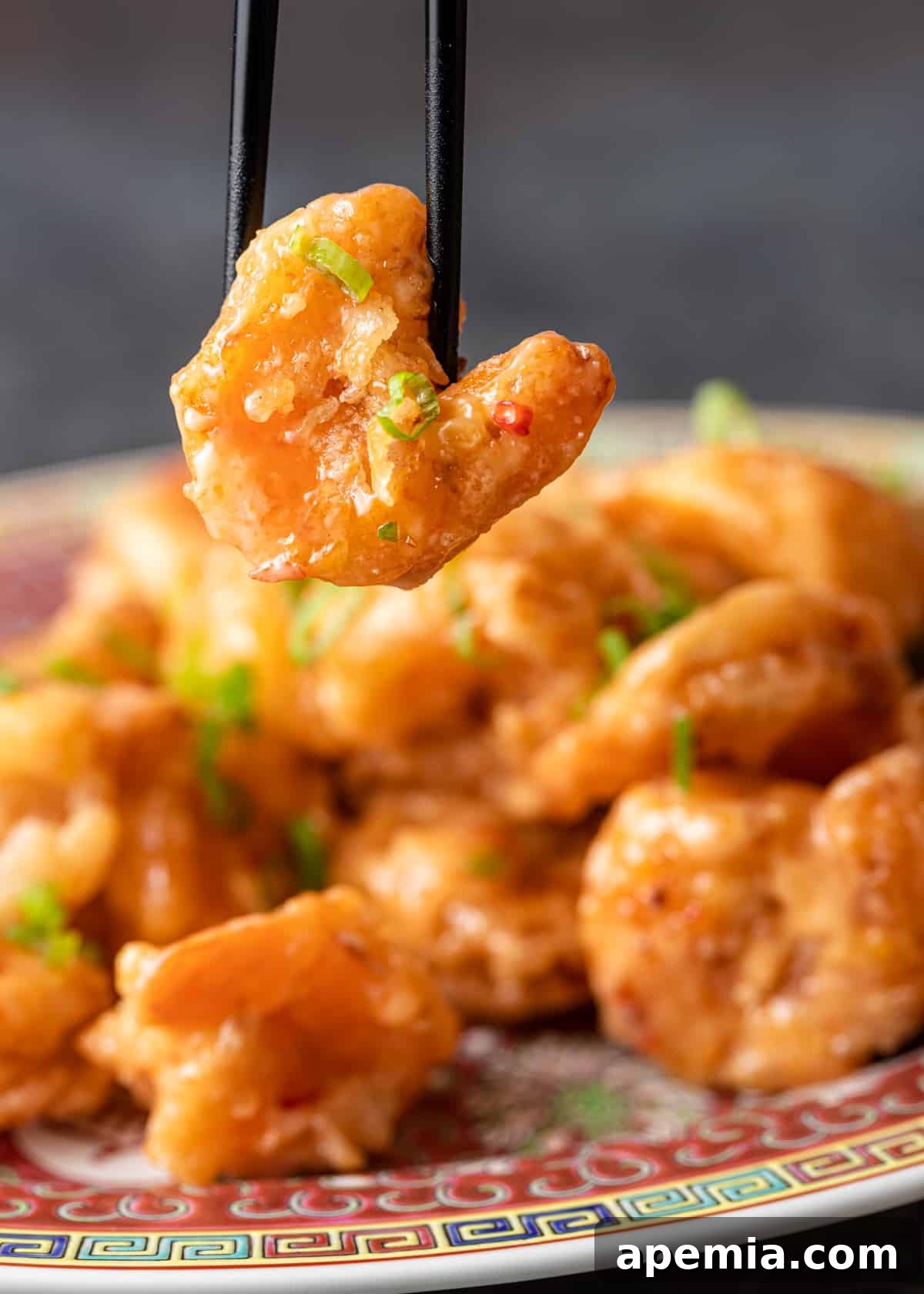 closeup: chopsticks holding bang bang shrimp over top of bang bang shrimp on colorful platter