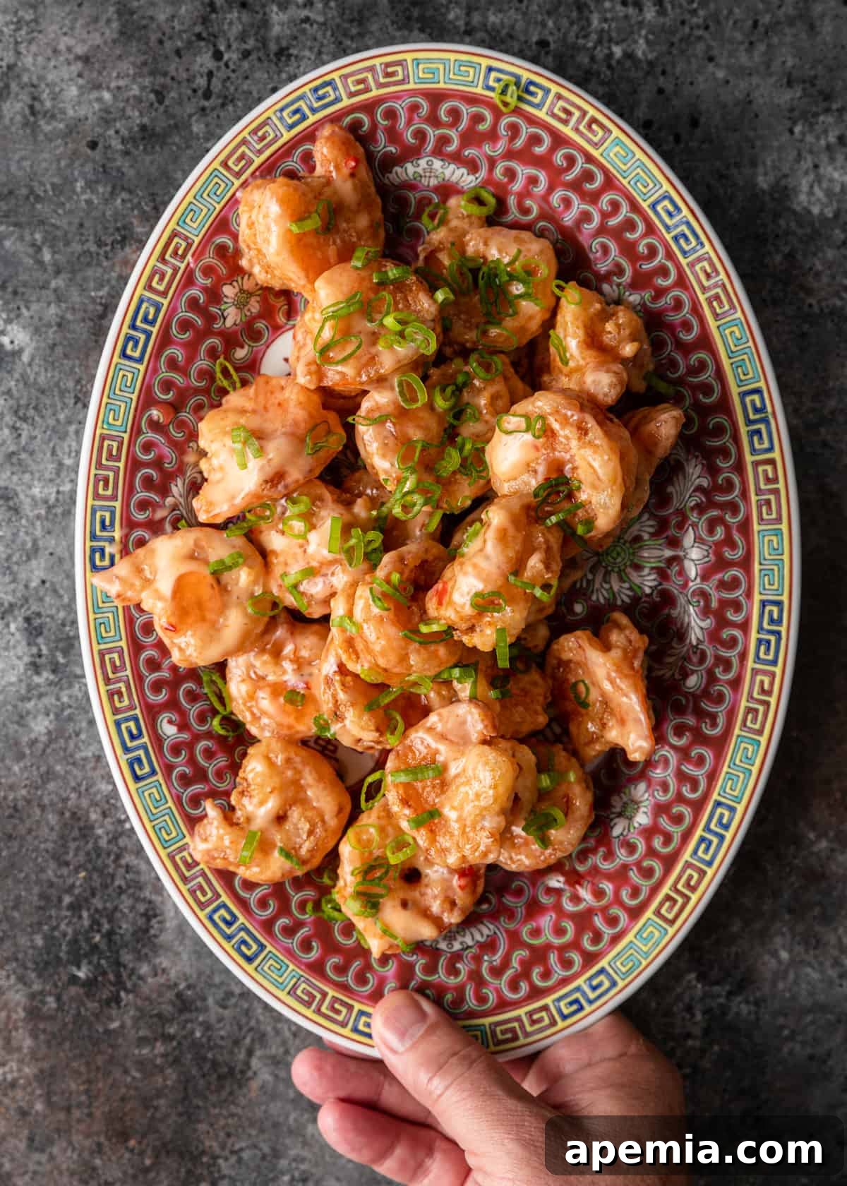 overhead: bang bang shrimp recipe on colorful platter on counter topped with sliced green onions