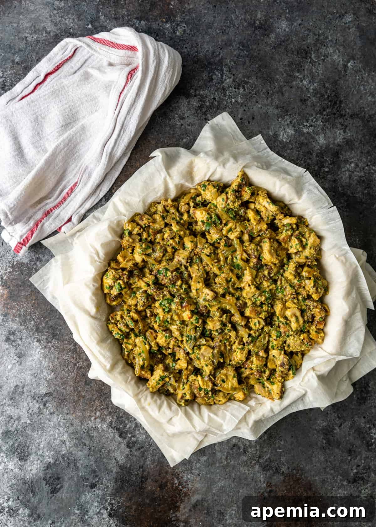 Process shot: Layering the savory spiced chicken filling evenly over the filo and almond layers in the pie dish.