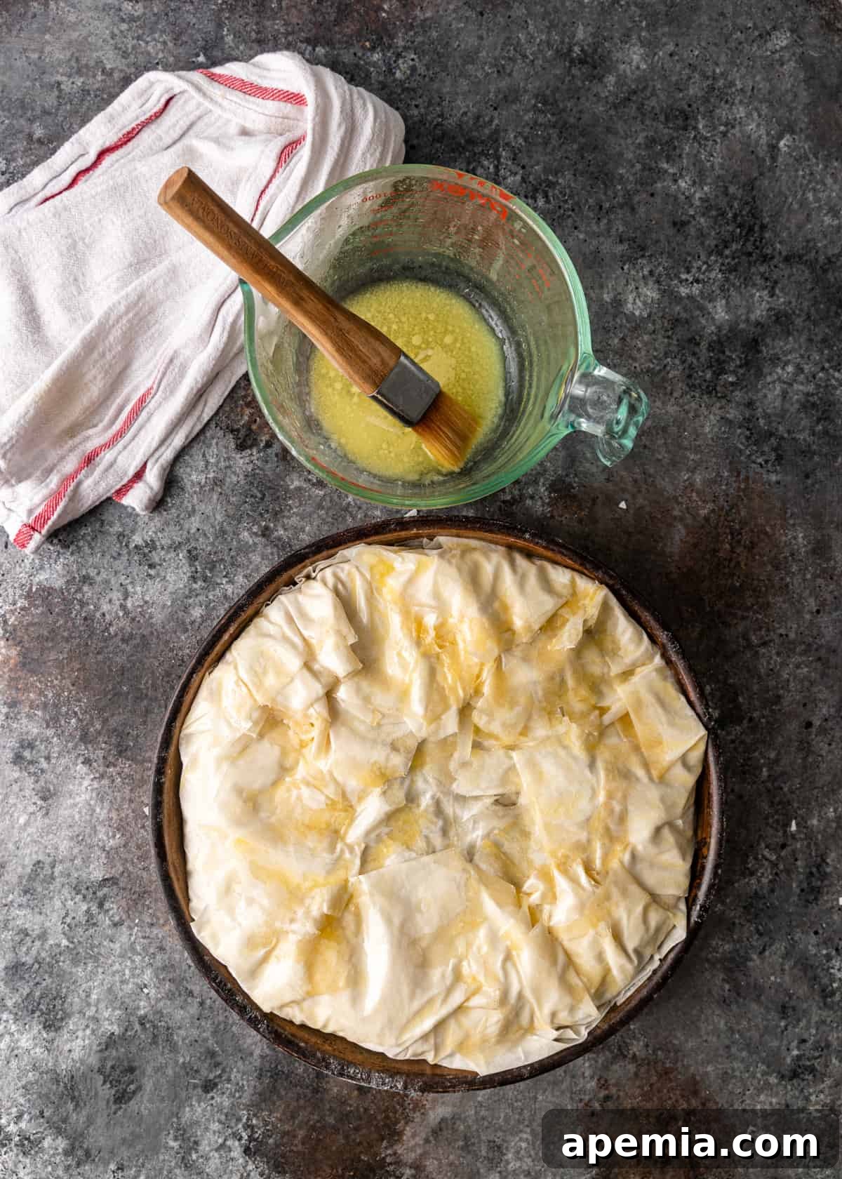Process shot: Brushing the top of the assembled pastilla with melted butter and egg wash for a golden crust.