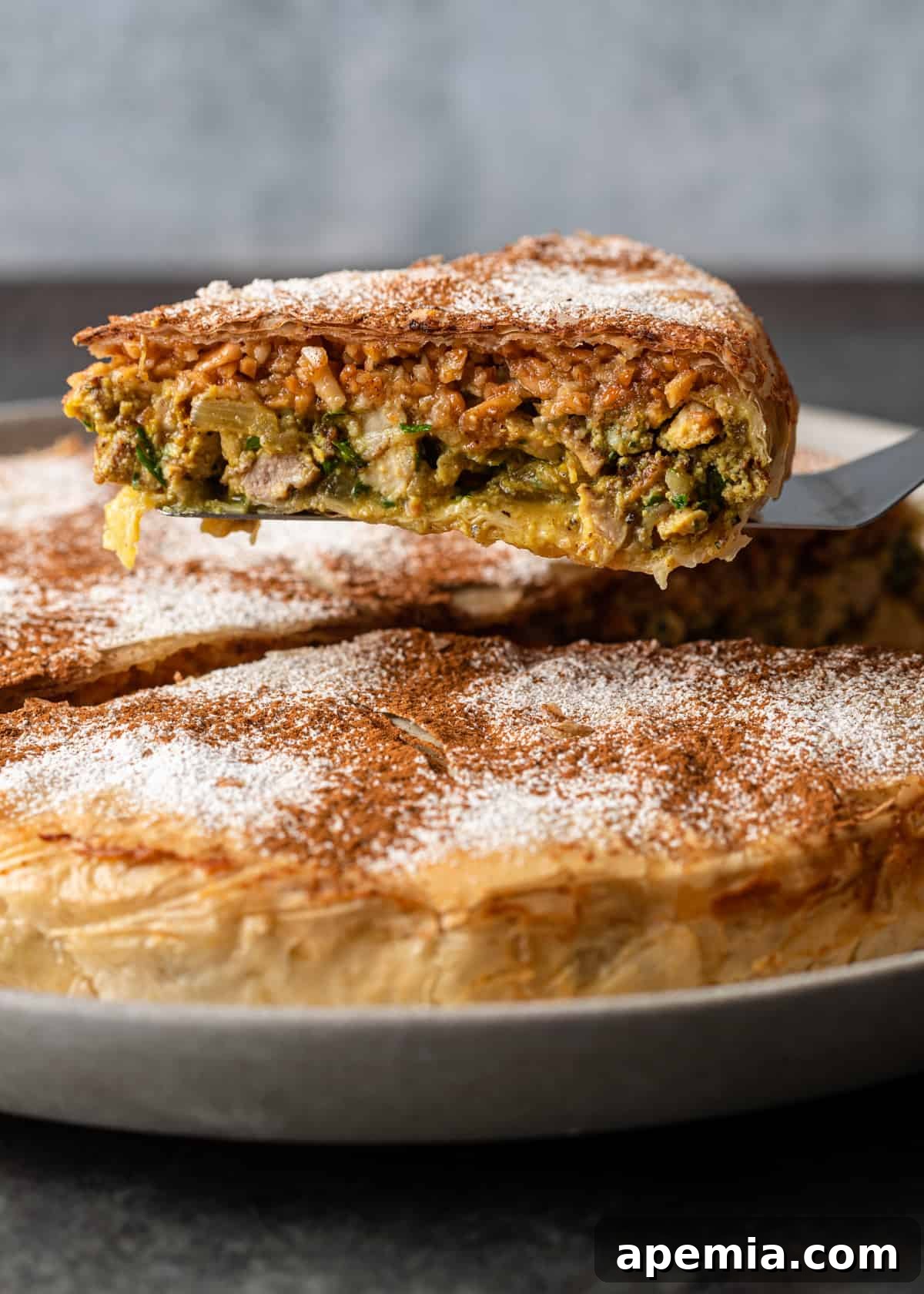A pie server lifting a perfectly cut slice of Pastilla, revealing the flavorful layers of chicken and almond filling within its flaky crust.