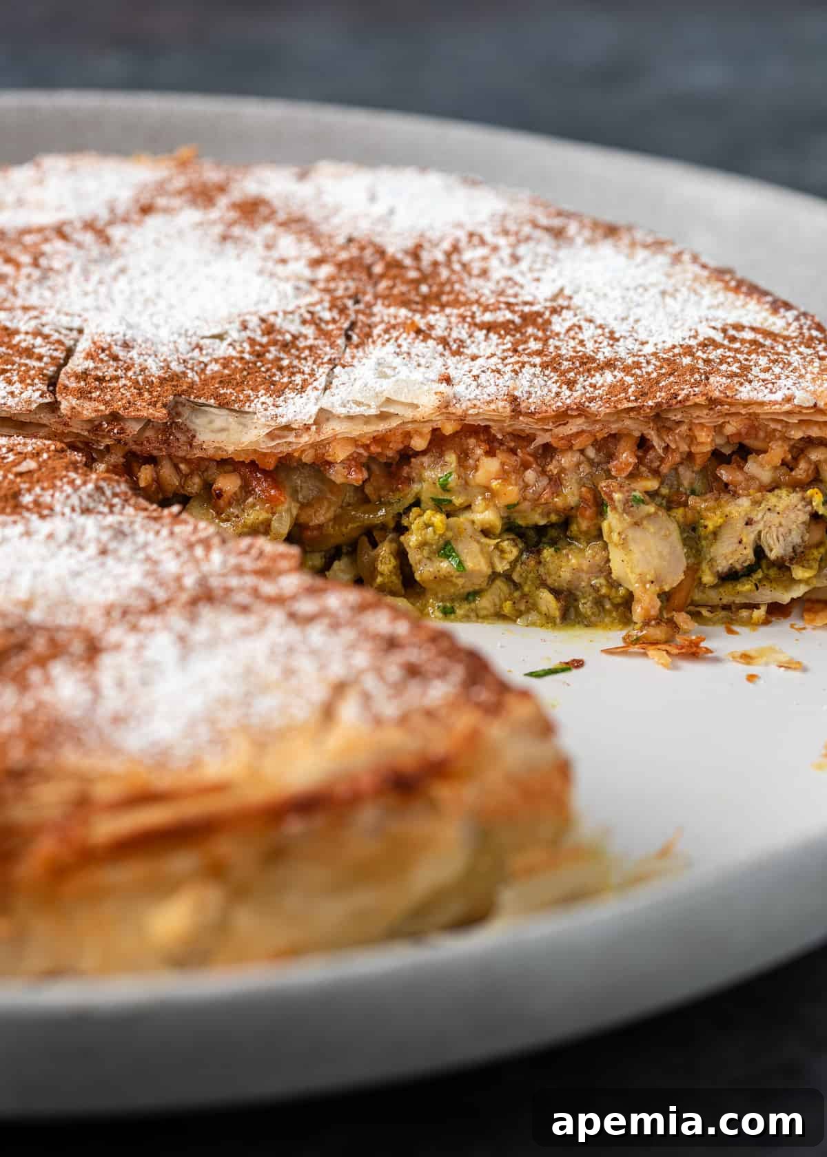 A close-up view of a baked Moroccan Pastilla on a white platter, with a perfect slice removed to showcase its layers.