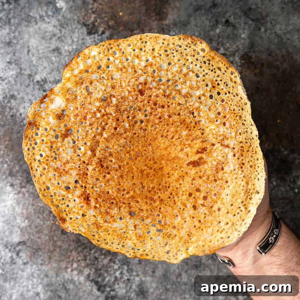overhead: a hand holding a golden crispy dosa crepe