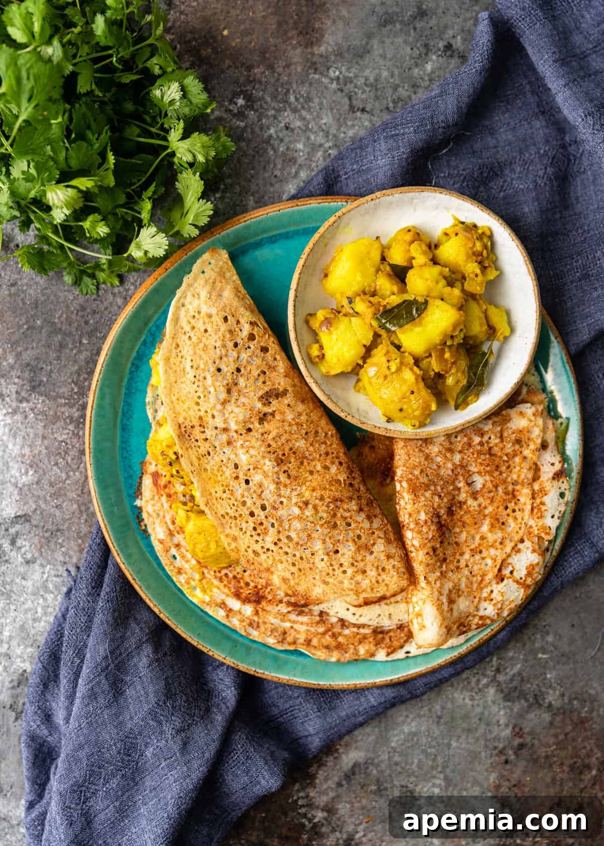 overhead: folded dosa on a green plate with a small bowl of potatoes