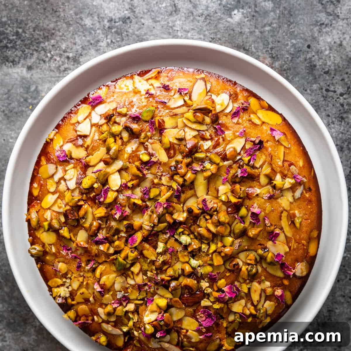Overhead shot of a beautifully decorated Persian love cake on a white plate, garnished with pistachios and rose petals.