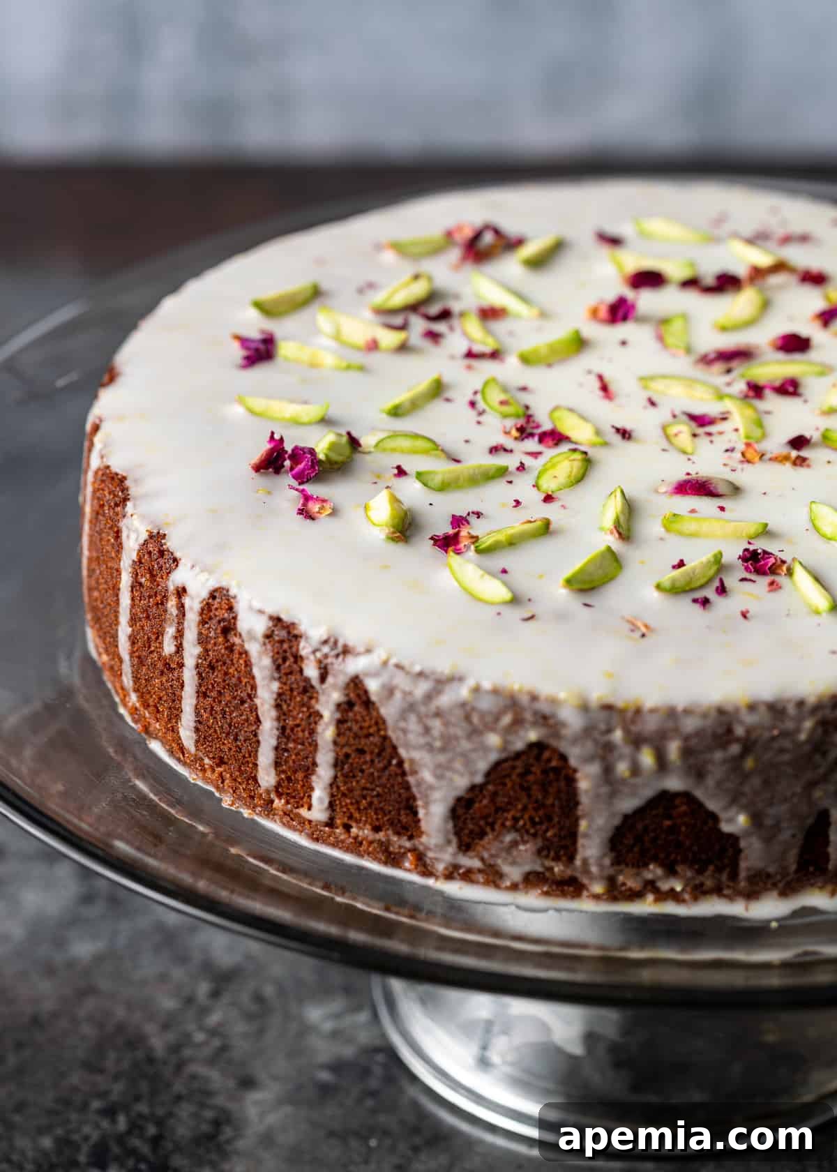 Closeup side view of a Persian Love Cake generously drizzled with white icing, presented on a clear serving platter.