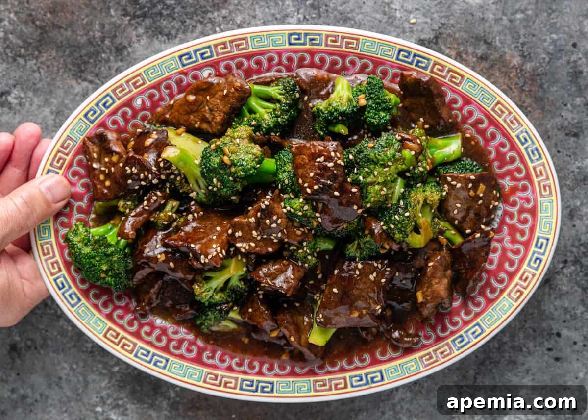 overhead shot of a hand holding a platter of broccoli beef on a kitchen counter