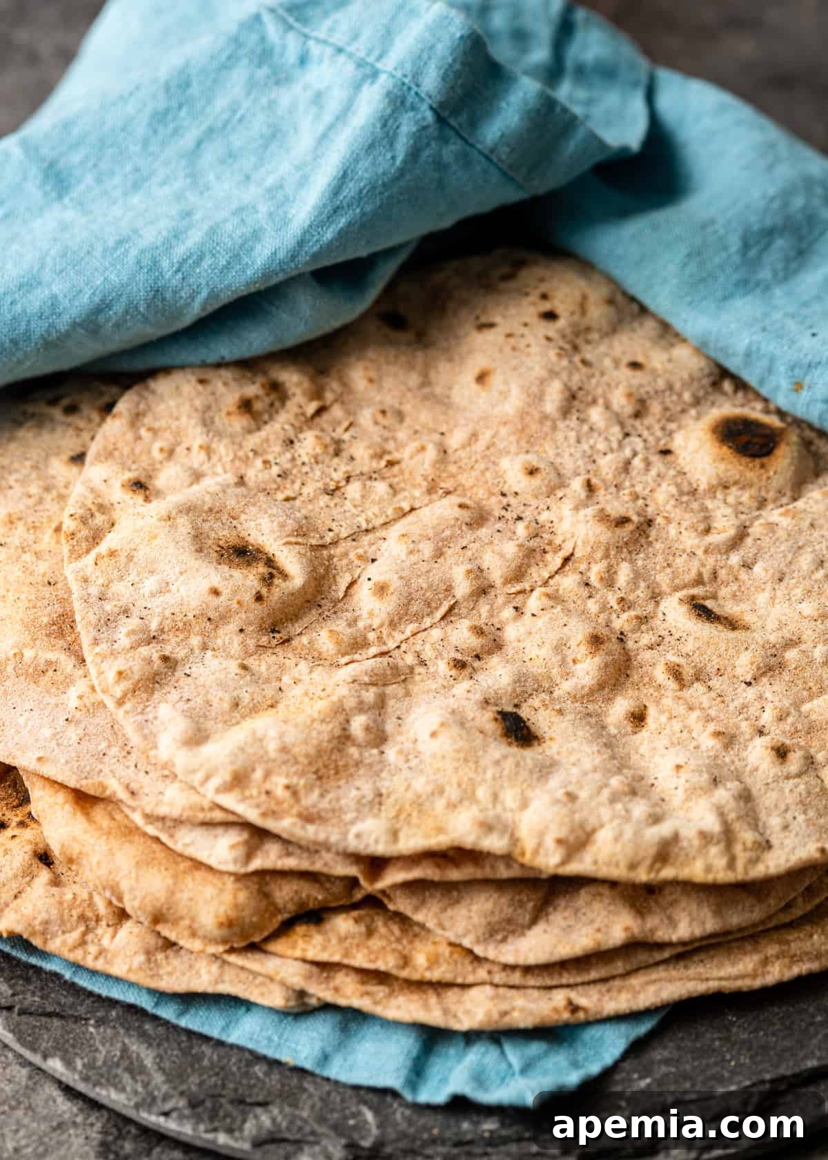 Chapati, an Indian flatbread, meticulously wrapped in a blue tea towel and placed on a kitchen counter