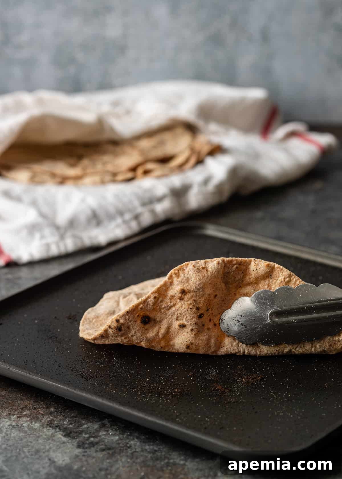 Closeup side view of tongs holding a browning Roti on a hot skillet, showcasing the early stages of cooking.