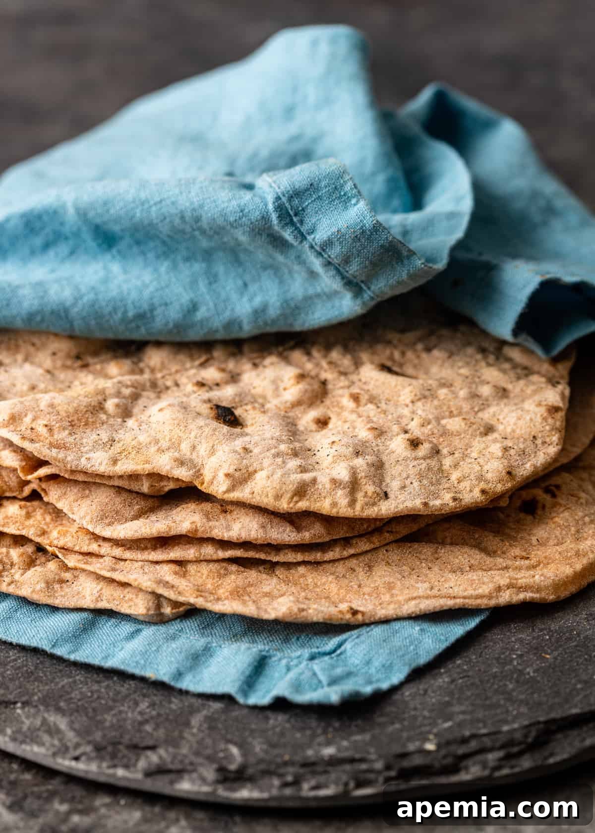 Closeup side view of Indian flatbread (Roti) elegantly wrapped in a blue tea towel, preserving its warmth and softness, ready to be served.