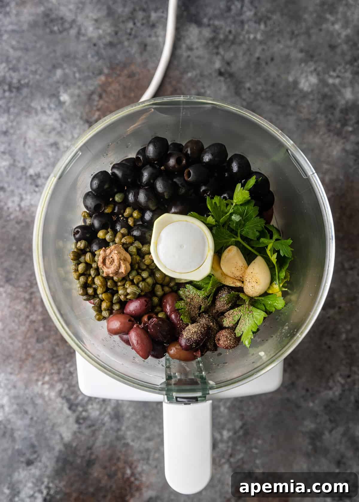 Savory Mediterranean Tapenade 5 Overhead process shot: Fresh herbs and a mix of green and black olives are placed inside a food processor bowl, ready for blending.