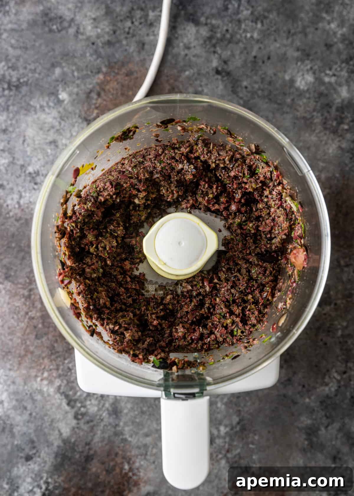 Savory Mediterranean Tapenade 6 Overhead process shot: The food processor is actively chopping the herbs and olives, creating a coarse mixture for the tapenade.