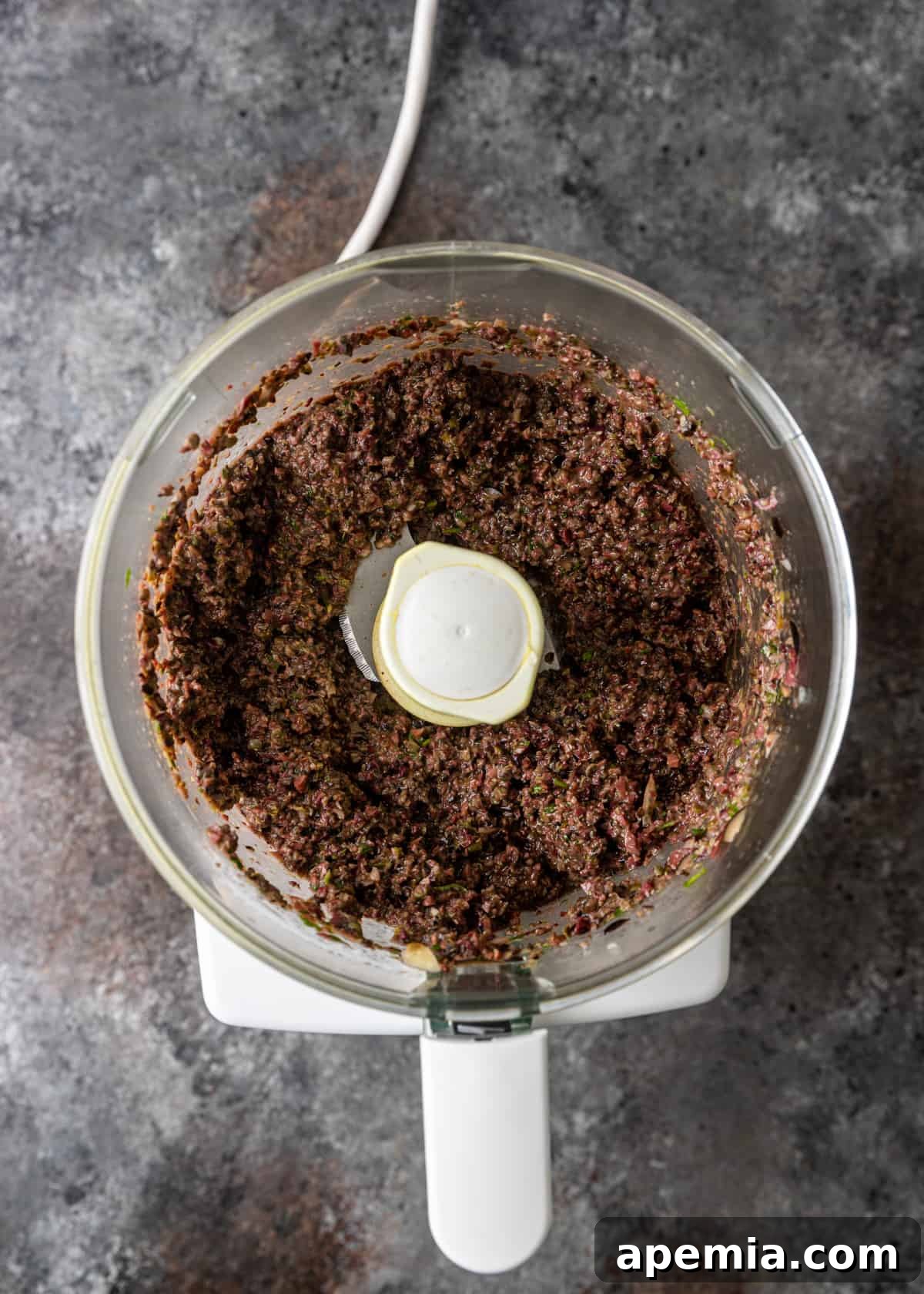 Savory Mediterranean Tapenade 7 Overhead process shot: The olive tapenade recipe is being made in a blender, showing the mixture forming into a chunky paste.