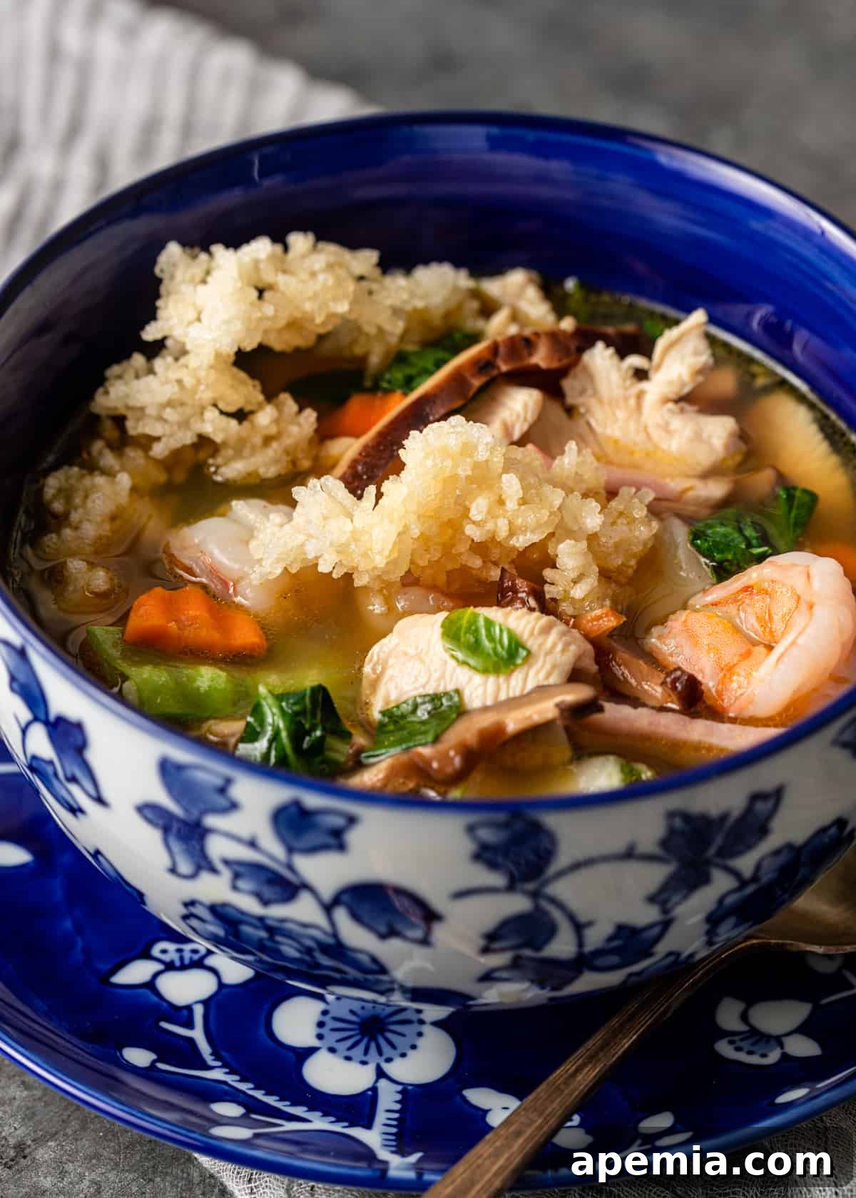Close-up of Sizzling Rice Soup, showcasing succulent mushrooms, plump shrimp, and an assortment of colorful vegetables in a blue and white bowl