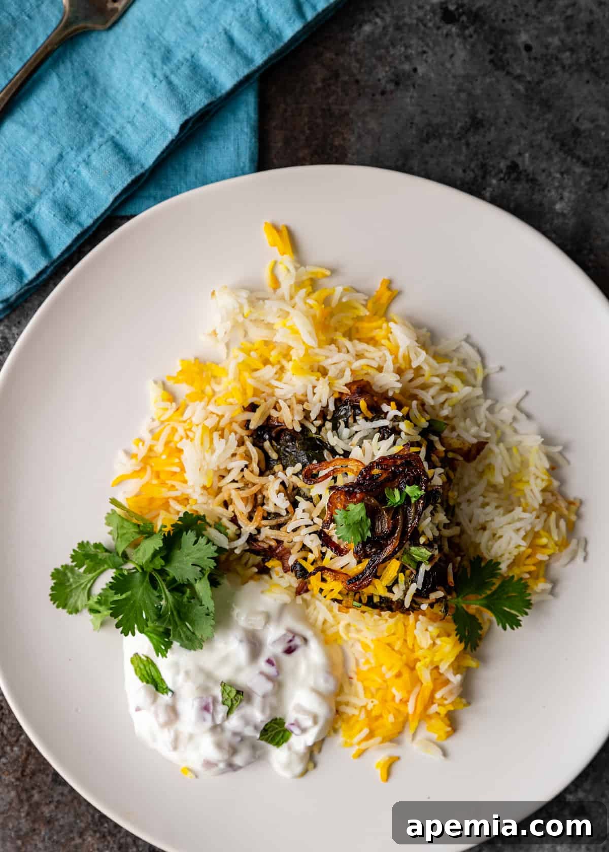 overhead: biryani on a white plate with tzaztiki