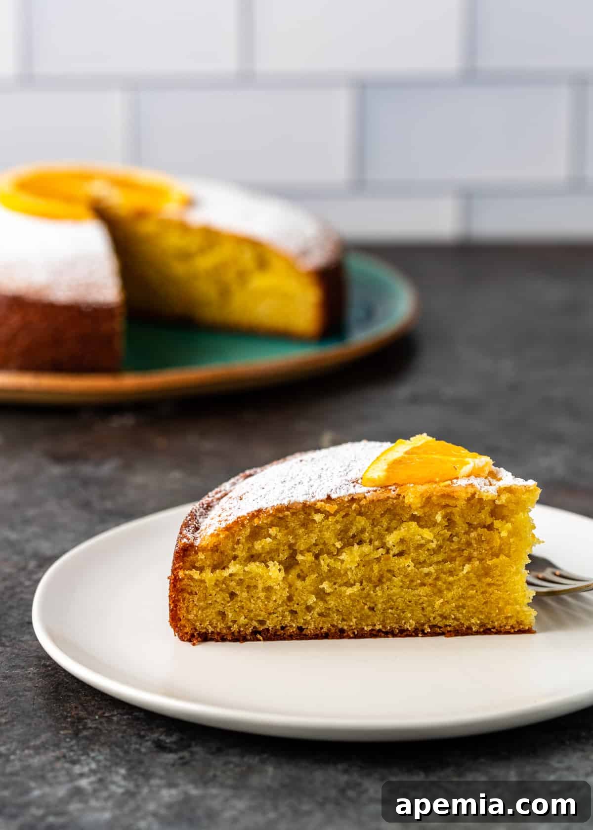 Closeup side view of a slice of olive oil cake on a pristine white plate, accompanied by a fork, ready to be enjoyed.