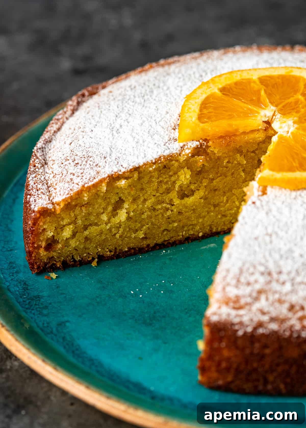 Closeup side view of a whole olive oil cake on a serving platter, with one slice already removed, highlighting its beautiful golden crust and soft interior.