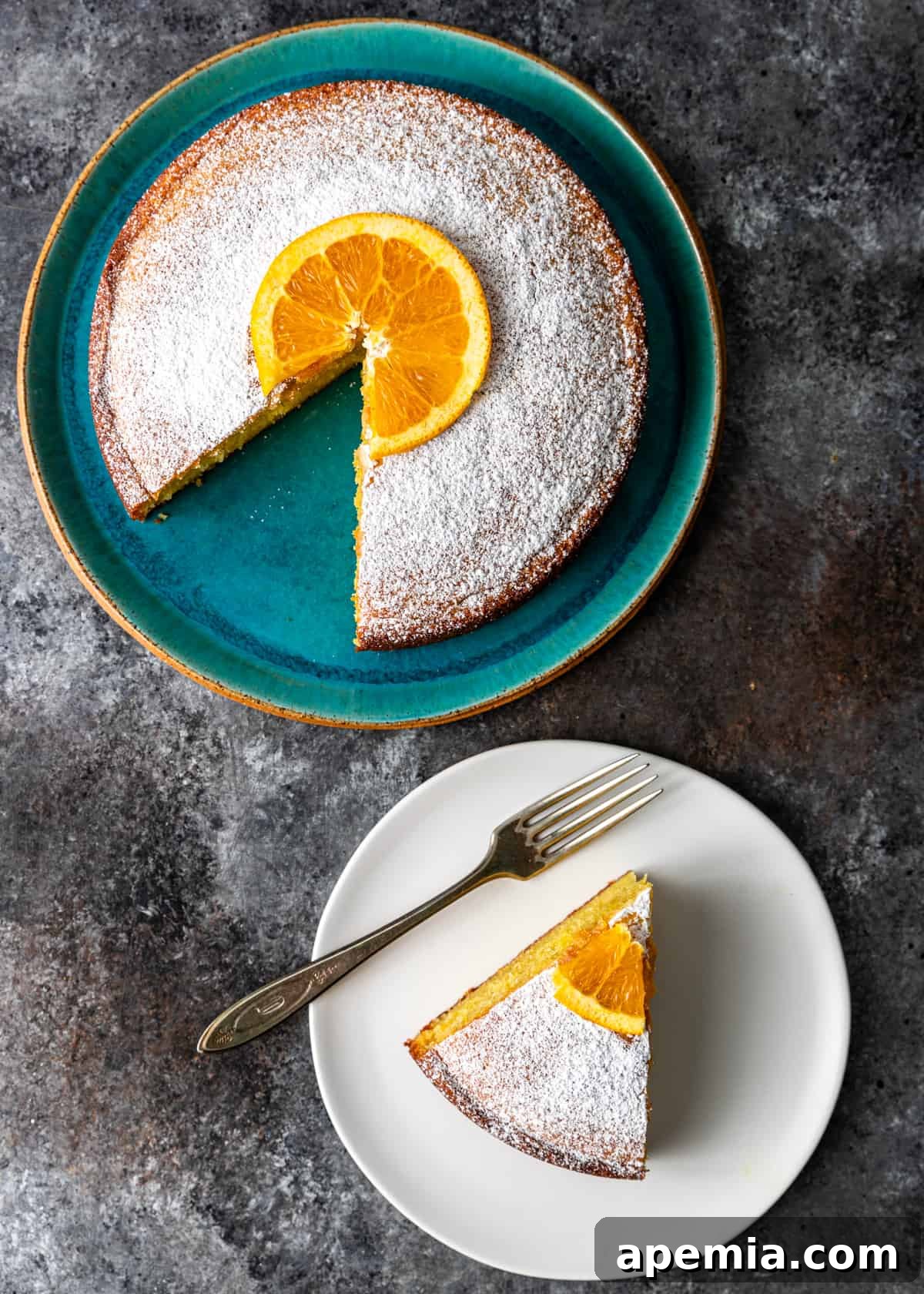 Overhead process shot: a white plate with a perfectly cut slice of olive oil cake and a fork, alongside the remaining cake on a larger platter, ready for serving.