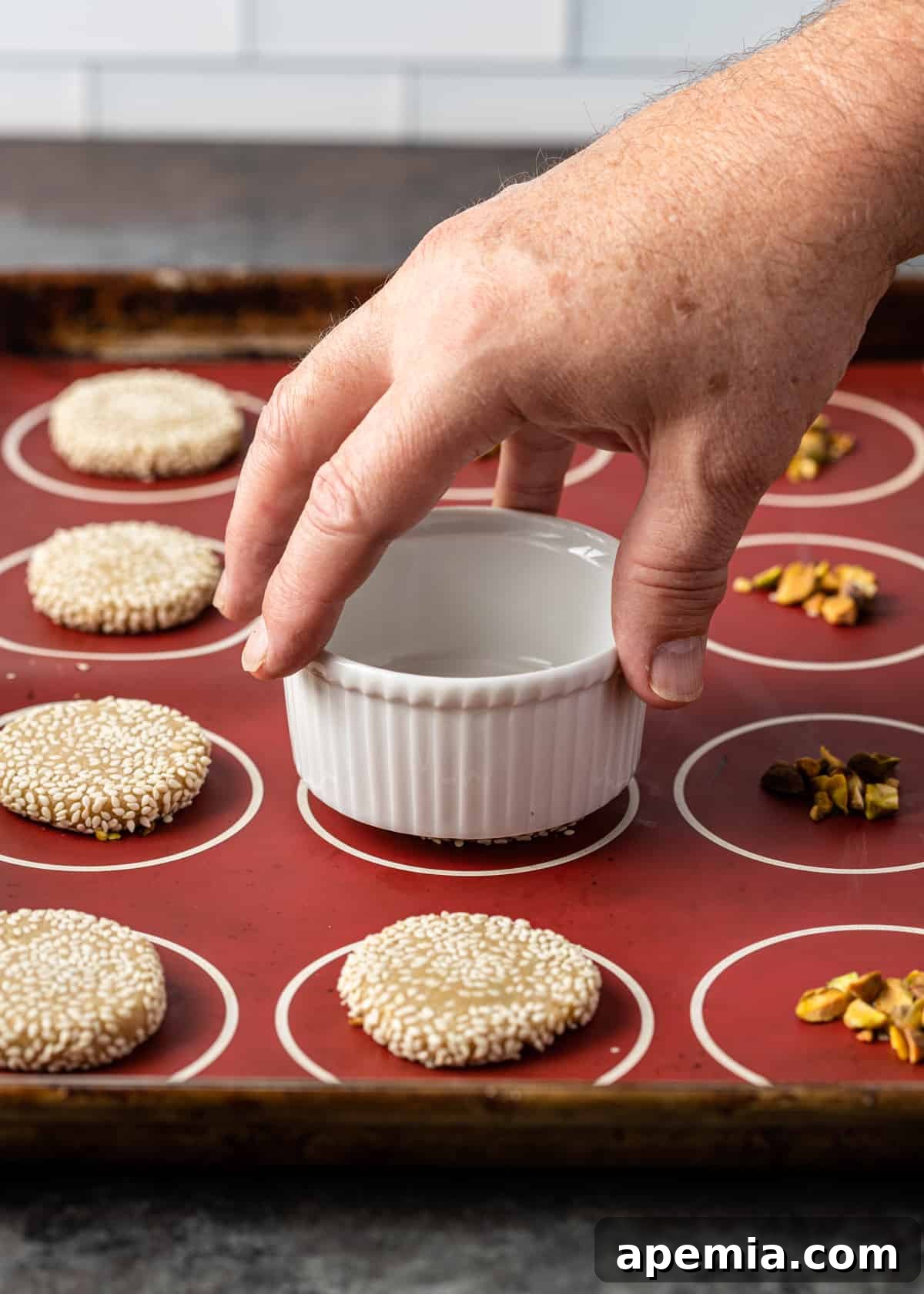 closeup side view process shot: hand holding small bowl flattening cookie dough