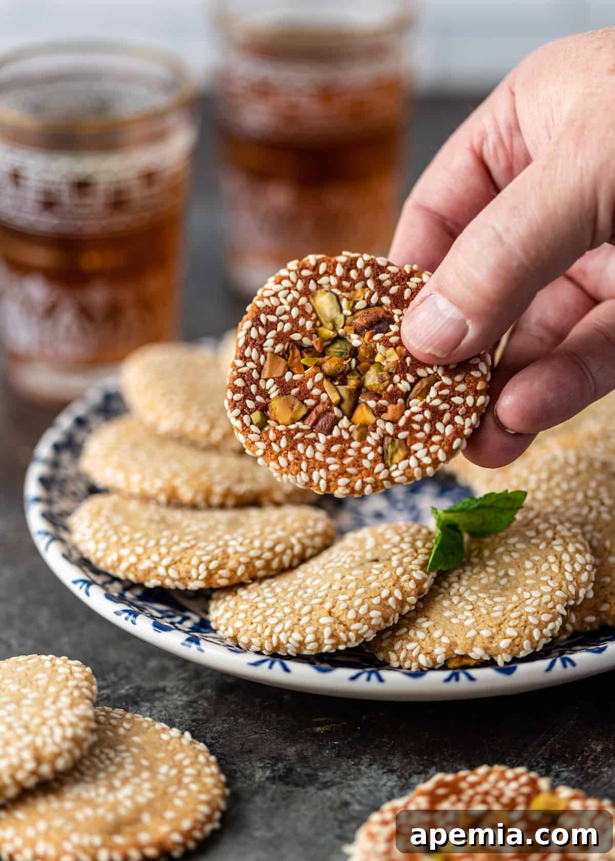 closeup side view: hand holding a sesame seed cookie in front of plate of cookies