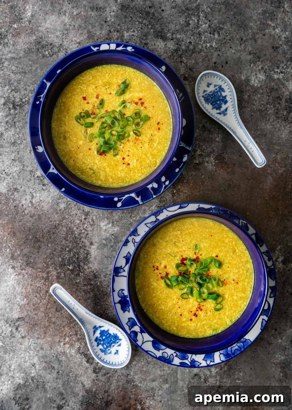 overhead: two blue bowls filled with egg flower soup on top of a white and blue plate with white and blue spoons on side