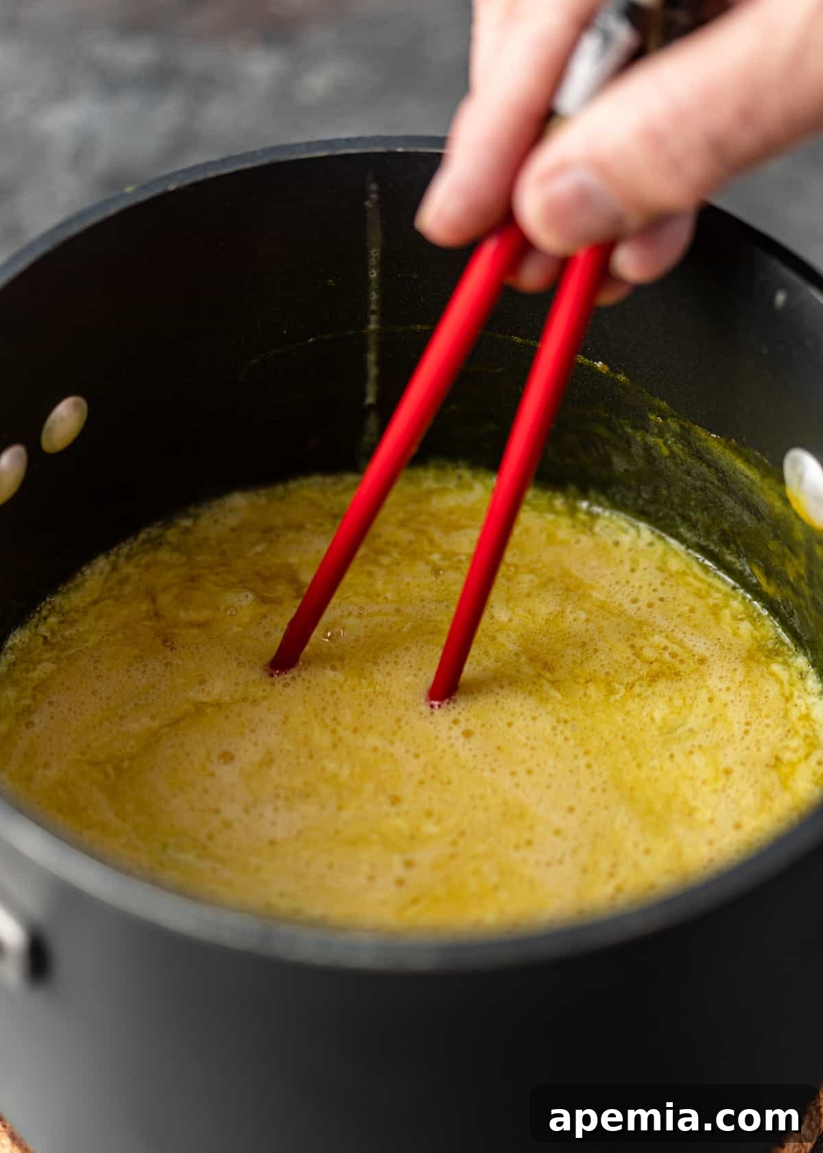 closeup side view: hand holding red chopsticks stirring egg drop soup