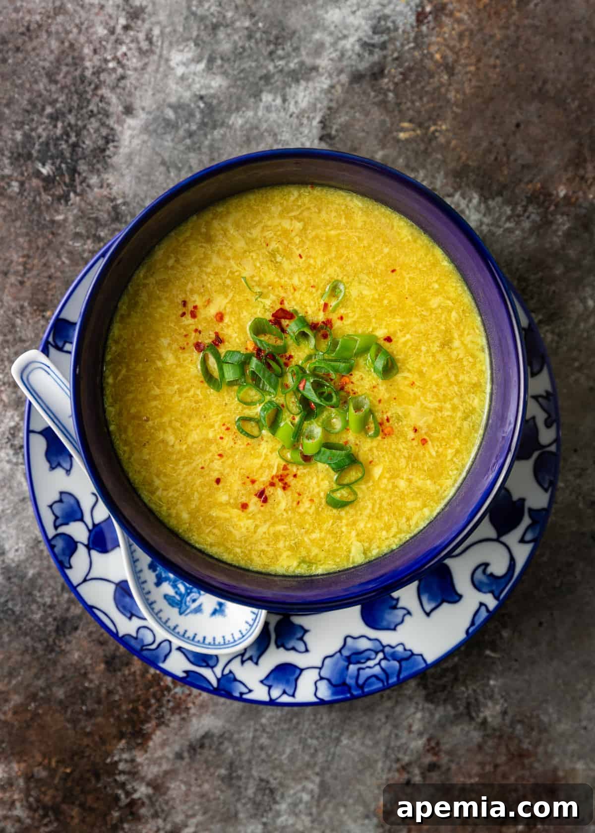 closeup overhead: egg flower soup in blue bowl topped with green onions