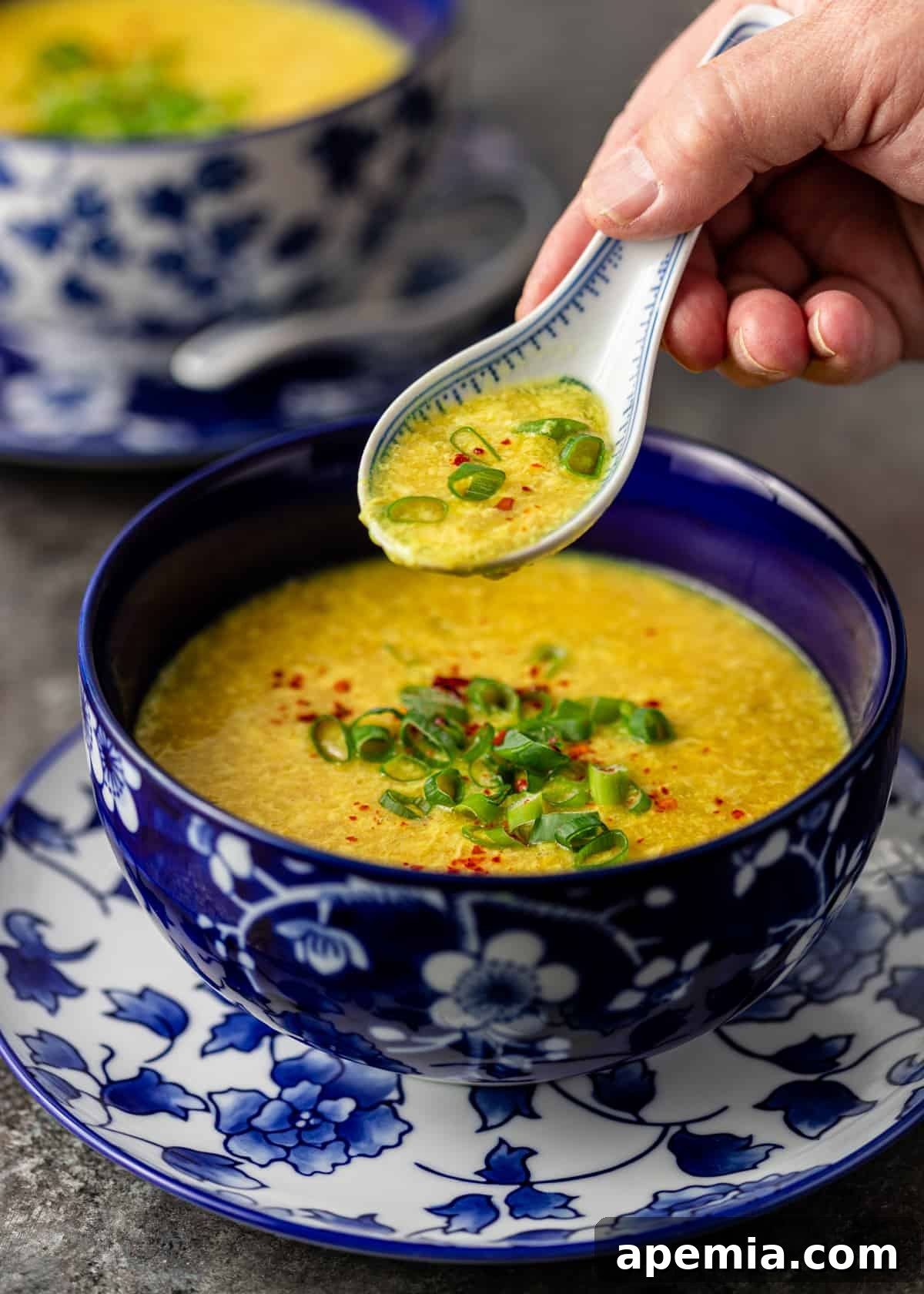 closeup side view: spoon with egg drop soup over top of blue bowl of egg flower soup