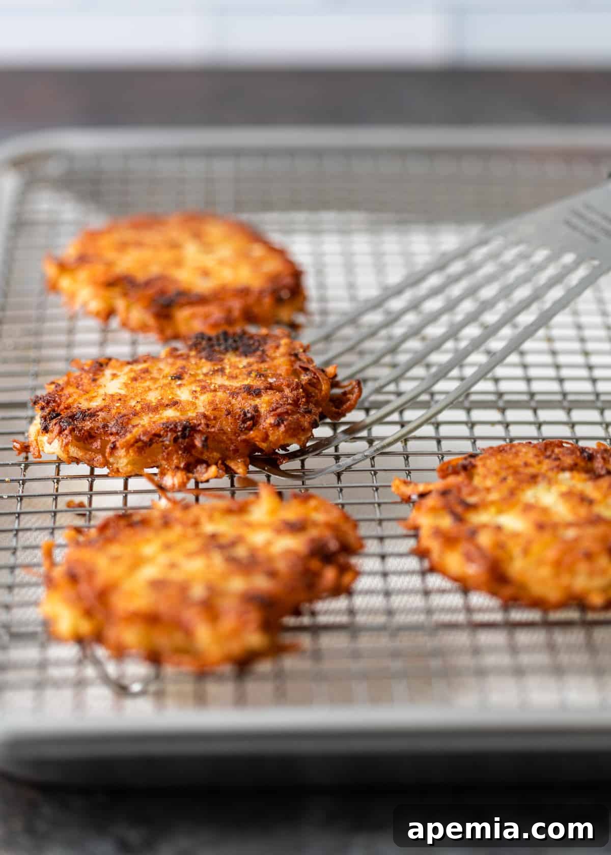 Overhead process shot of freshly fried potato latkes being placed on a cooling rack, allowing excess grease to drain for maximum crispness.