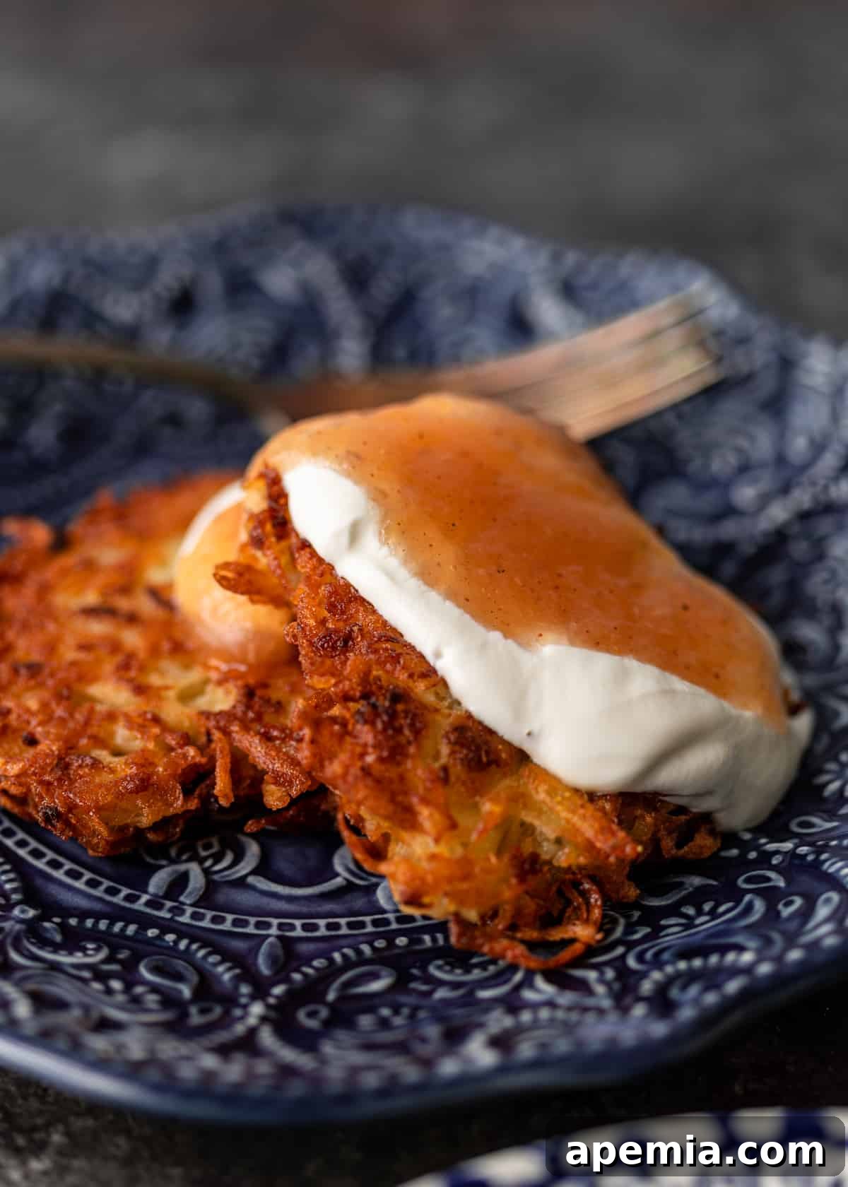 Closeup side view of a single latke recipe served elegantly on a dark blue plate, highlighting its golden texture and potential toppings.